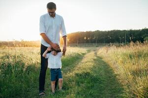 hermoso papá con su pequeño linda hijo son teniendo divertido y jugando en verde herboso césped. contento familia concepto. belleza naturaleza escena con familia al aire libre estilo de vida. familia descansando juntos. padres día. foto