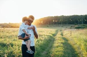 hermoso papá con su pequeño linda hijo son teniendo divertido y jugando en verde herboso césped. contento familia concepto. belleza naturaleza escena con familia al aire libre estilo de vida. familia descansando juntos. padres día. foto