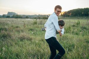 hermoso papá con su pequeño linda hijo son teniendo divertido y jugando en verde herboso césped. contento familia concepto. belleza naturaleza escena con familia al aire libre estilo de vida. familia descansando juntos. padres día. foto