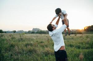 hermoso papá con su pequeño linda hijo son teniendo divertido y jugando en verde herboso césped. contento familia concepto. belleza naturaleza escena con familia al aire libre estilo de vida. familia descansando juntos. padres día. foto