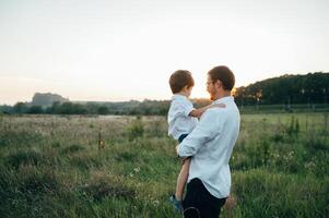 hermoso papá con su pequeño linda hijo son teniendo divertido y jugando en verde herboso césped. contento familia concepto. belleza naturaleza escena con familia al aire libre estilo de vida. familia descansando juntos. padres día. foto