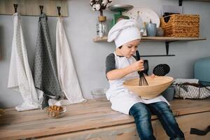 joven chico linda en el cocina cocinar cocinero en blanco uniforme y sombrero cerca mesa. Navidad hecho en casa pan de jengibre. el chico cocido el chocolate galletas. foto