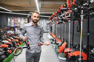 happy customer with electric lawn trimmer in hands at garden equipment store photo