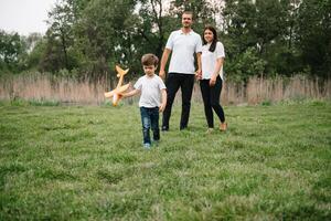 Father, mother and son playing with toy airplane in the park. friendly family. People having fun outdoors. Picture made on the background of the park and blue sky. concept of a happy family photo