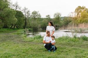 contento familia madre padre y niño hijo en naturaleza en puesta de sol. mamá, papá y niño riendo y abrazando, disfrutando naturaleza afuera. soleado día, bueno humor. concepto de un contento familia. foto