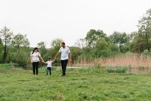 contento familia madre padre y niño hijo en naturaleza en puesta de sol. mamá, papá y niño riendo y abrazando, disfrutando naturaleza afuera. soleado día, bueno humor. concepto de un contento familia. foto