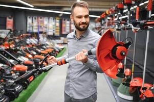 happy customer with electric lawn trimmer in hands at garden equipment store photo