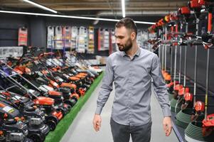 happy customer with electric lawn trimmer in hands at garden equipment store photo