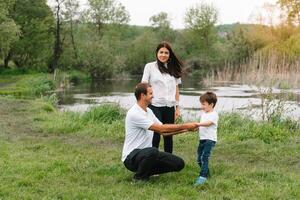 contento familia madre padre y niño hijo en naturaleza en puesta de sol. mamá, papá y niño riendo y abrazando, disfrutando naturaleza afuera. soleado día, bueno humor. concepto de un contento familia. foto