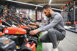 Young man buys a new lawnmower in a garden supplies store photo