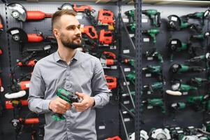 un hombre en un hardware Tienda elige un nuevo destornillador siguiente a un escaparate de poder herramientas foto