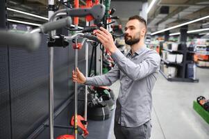 customer with electric lawn trimmer in hands at garden equipment store photo