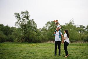 contento familia madre padre y niño hijo en naturaleza en puesta de sol. mamá, papá y niño riendo y abrazando, disfrutando naturaleza afuera. soleado día, bueno humor. concepto de un contento familia. foto