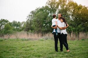 contento familia madre padre y niño hijo en naturaleza en puesta de sol. mamá, papá y niño riendo y abrazando, disfrutando naturaleza afuera. soleado día, bueno humor. concepto de un contento familia. foto