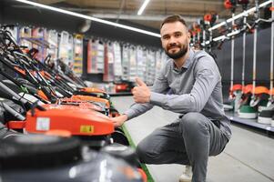 Young man buys a new lawnmower in a garden supplies store photo