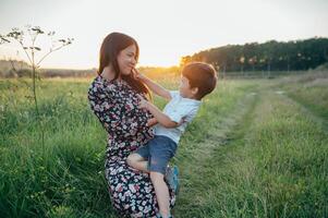 elegante madre y hermoso hijo teniendo divertido en el naturaleza. contento familia concepto. belleza naturaleza escena con familia al aire libre estilo de vida. contento familia descansando juntos. felicidad en familia vida. madres día foto