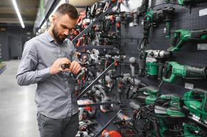 un hombre en un hardware Tienda elige un nuevo destornillador siguiente a un escaparate de poder herramientas foto