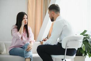 Psychologist taking notes during therapy session with sad young woman in his office. Copy space photo