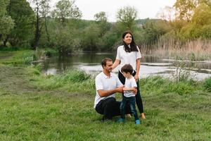 contento familia madre padre y niño hijo en naturaleza en puesta de sol. mamá, papá y niño riendo y abrazando, disfrutando naturaleza afuera. soleado día, bueno humor. concepto de un contento familia. foto