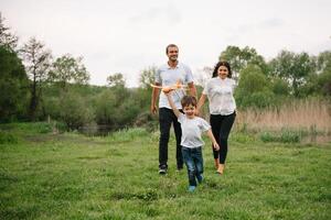 padre, madre y hijo jugando con juguete avión en el parque. simpático familia. personas teniendo divertido al aire libre. imagen hecho en el antecedentes de el parque y azul cielo. concepto de un contento familia foto