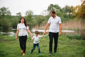 contento familia madre padre y niño hijo en naturaleza en puesta de sol. mamá, papá y niño riendo y abrazando, disfrutando naturaleza afuera. soleado día, bueno humor. concepto de un contento familia foto