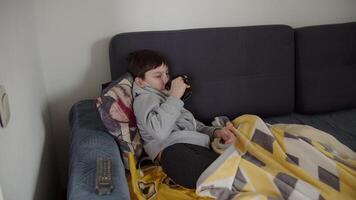 Schoolboy lies in bed with a mask on face and drinks tea, child is sick at home video