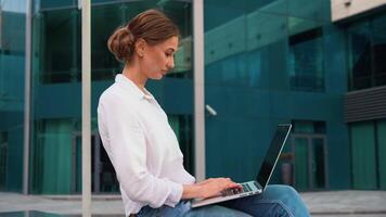 Smiling businesswoman working on laptop outside modern office video