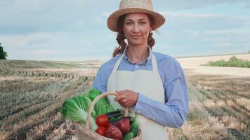 sonriente mujer granjero participación cesta lleno de vegetales en pie en campo video