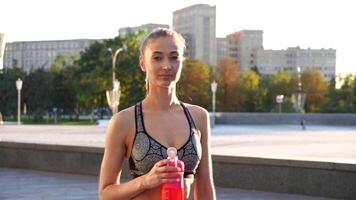 kvinna joggare innehav vatten flaska i stad parkera på solig dag video