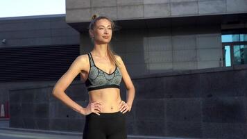sonriente joven hembra atleta en pie en contra urbano edificio video