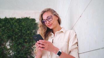 Smiling woman using smartphone leaning on white wall video