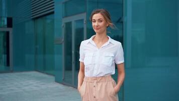 confidente mujer de negocios sonriente con manos en bolsillos fuera de oficina edificio video