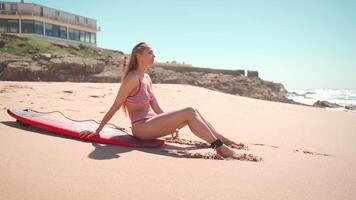 a woman sitting on the beach with a surfboard video