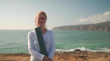 a woman in glasses holding a yoga mat by the ocean video