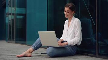 uma mulher sentado em a terra com dela computador portátil video