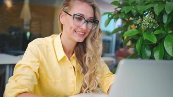 a woman in glasses sitting in a cafe with a laptop video