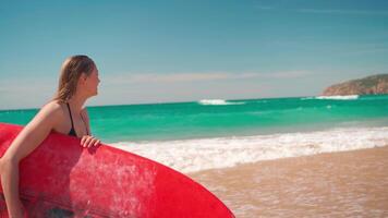 un' donna è in piedi su il spiaggia con un' rosso tavola da surf video