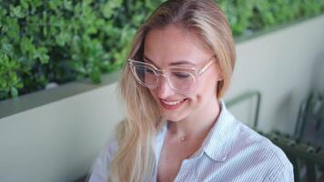 une femme dans des lunettes séance dans une café avec une portable video