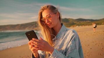 lado ver de joven mujer con rubio pelo mensajes de texto en teléfono inteligente a playa. video