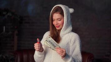 Beautiful young female dressed white hoodie with ears holds money in hand and sets fire to their lighter. video