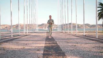 Young adult fitness woman jogging by embankment area coastal city in beautiful sunny day. video