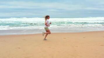zumbido aéreo imágenes Delgado rubia mujer corriendo Oceano playa. video