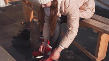 jong vrouw voorbereidingen treffen het schaatsen. Kaukasisch vrouw koppelverkoop schoenveters van ijs skates zittend bank buitenshuis. video