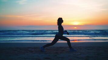 en kvinna håller på med yoga på de strand på solnedgång video
