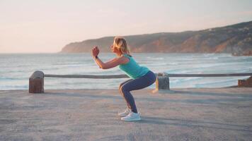 jong fit vrouw aan het doen hurken strand met zonsondergang video
