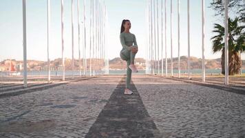 Fitness woman in sports wear doing lunges on step, and stretching legs on summer park near seaside. video