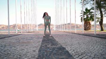 Fitness woman in sports wear doing lunges on step, and stretching legs on summer park near seaside. video