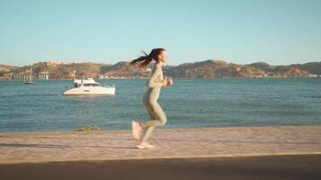 Young adult fitness woman jogging by embankment area coastal city in beautiful sunny day. video