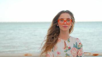 une femme dans des lunettes de soleil et une floral chemise des stands par le océan video