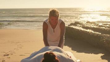 Woman enjoying professional spa hand massage lying on special table on beach during vacation. Massage therapist giving relaxing massage client's arms and shoulders video